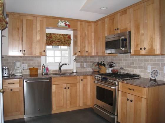 Gray stone floors, black countertops and a stainless steel cylindrical hood  contrast the warm, traditional maple cabinetry