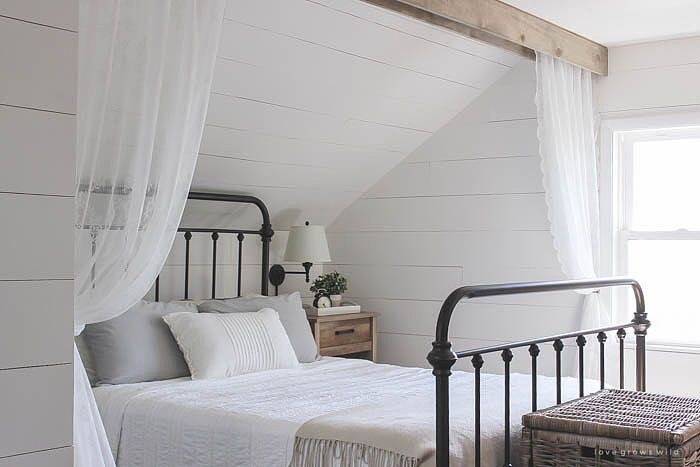 Love a pop of red pillows against the white shiplap bedroom walls and the traditional black wrought iron bed